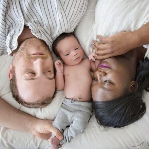 parents lying on a bed with a baby laying between their heads